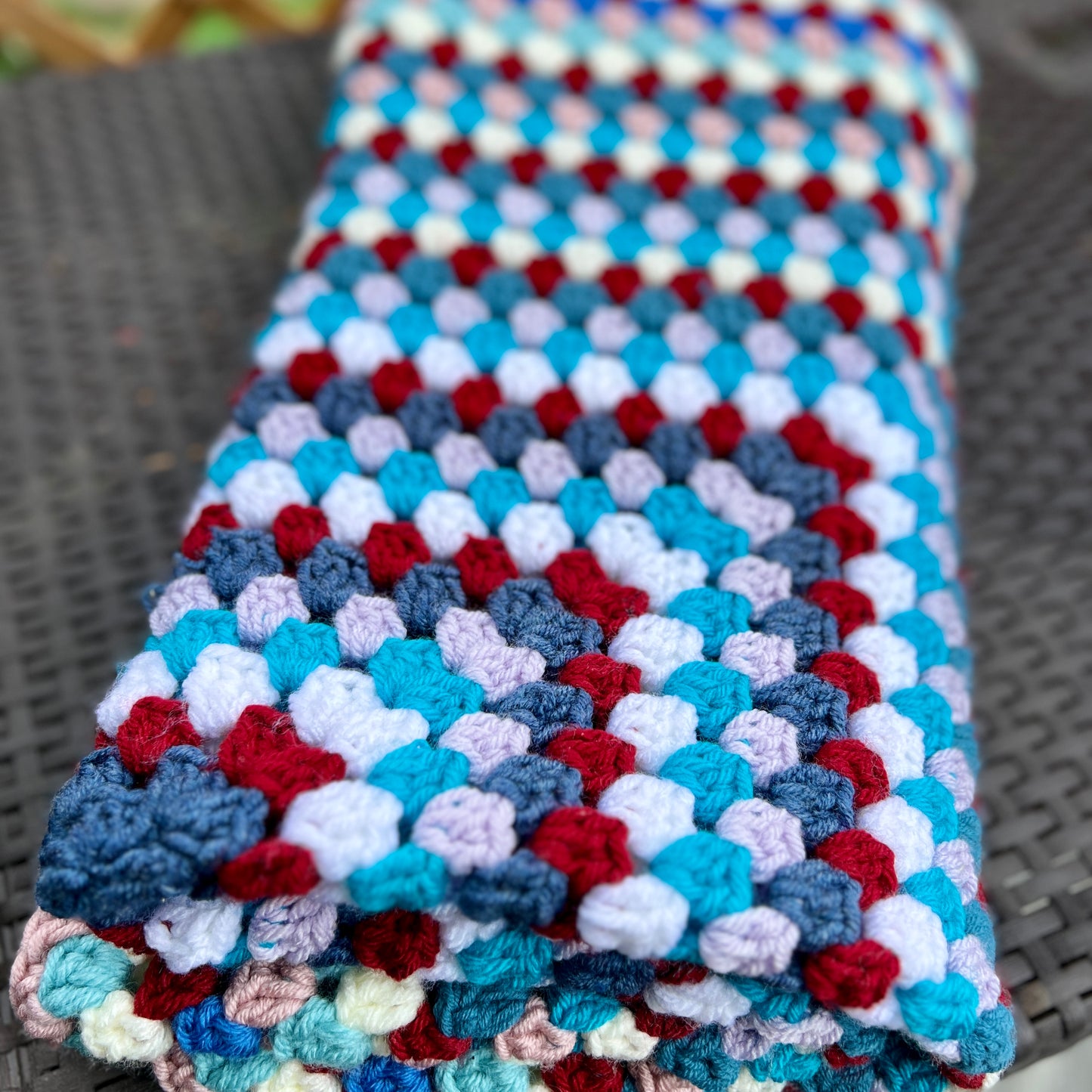 Colorful crocheted blanket with red, blue, and white pattern on a textured surface.