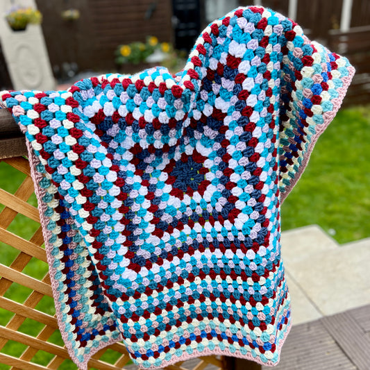 Colorful crocheted blanket on a wooden chair outdoors