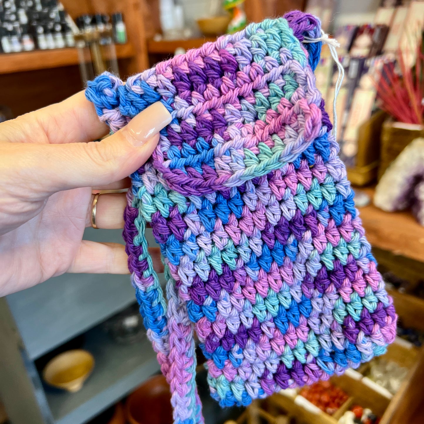 Multicolored crocheted fabric held by a hand in an indoor setting.