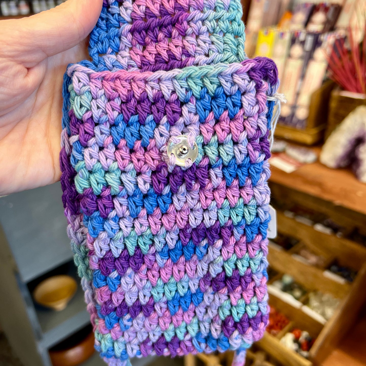 Handmade crochet phone case with a button held in a hand, with a blurred background of a store.